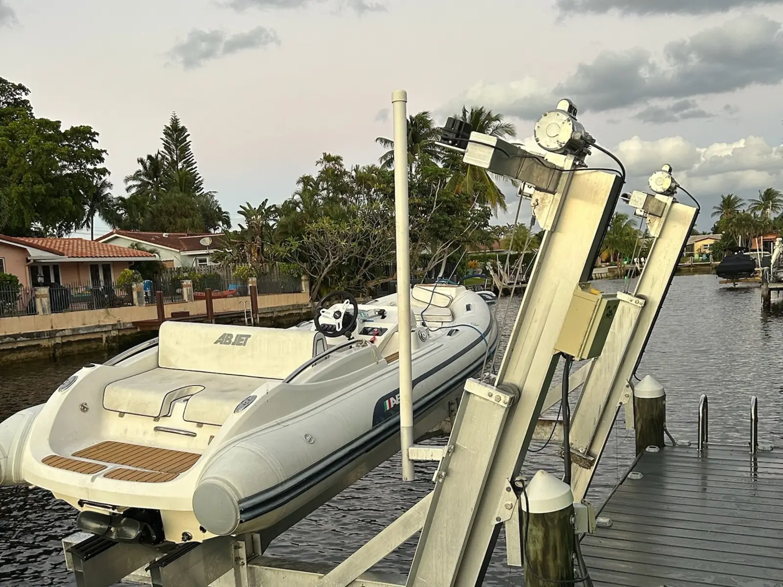 Aluminum elevator boat lift on a composite dock holding a white rigid inflatable tender, with the lift motors, cable sheaves, and an electrical box at the top of the angled columns