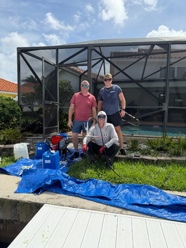 Three-person South Florida Seawall crew with NCFI injection pump, drums, and hoses beside a Boca Raton seawall