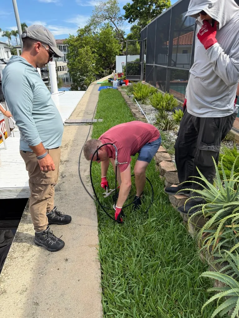 Technician driving a polyurethane injection probe into the lawn beside a Boca Raton concrete seawall cap