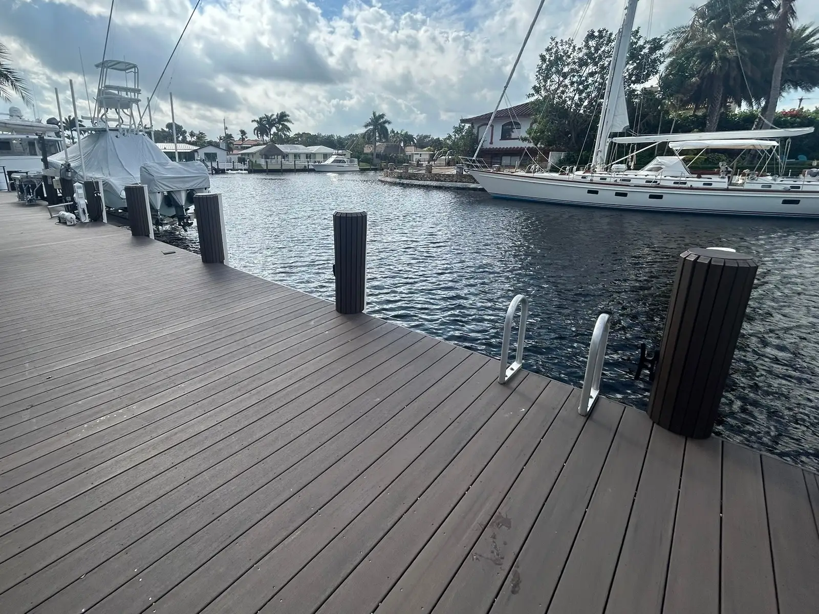 Composite dock on a South Florida canal with dark clad pilings along its edge and boats moored beyond