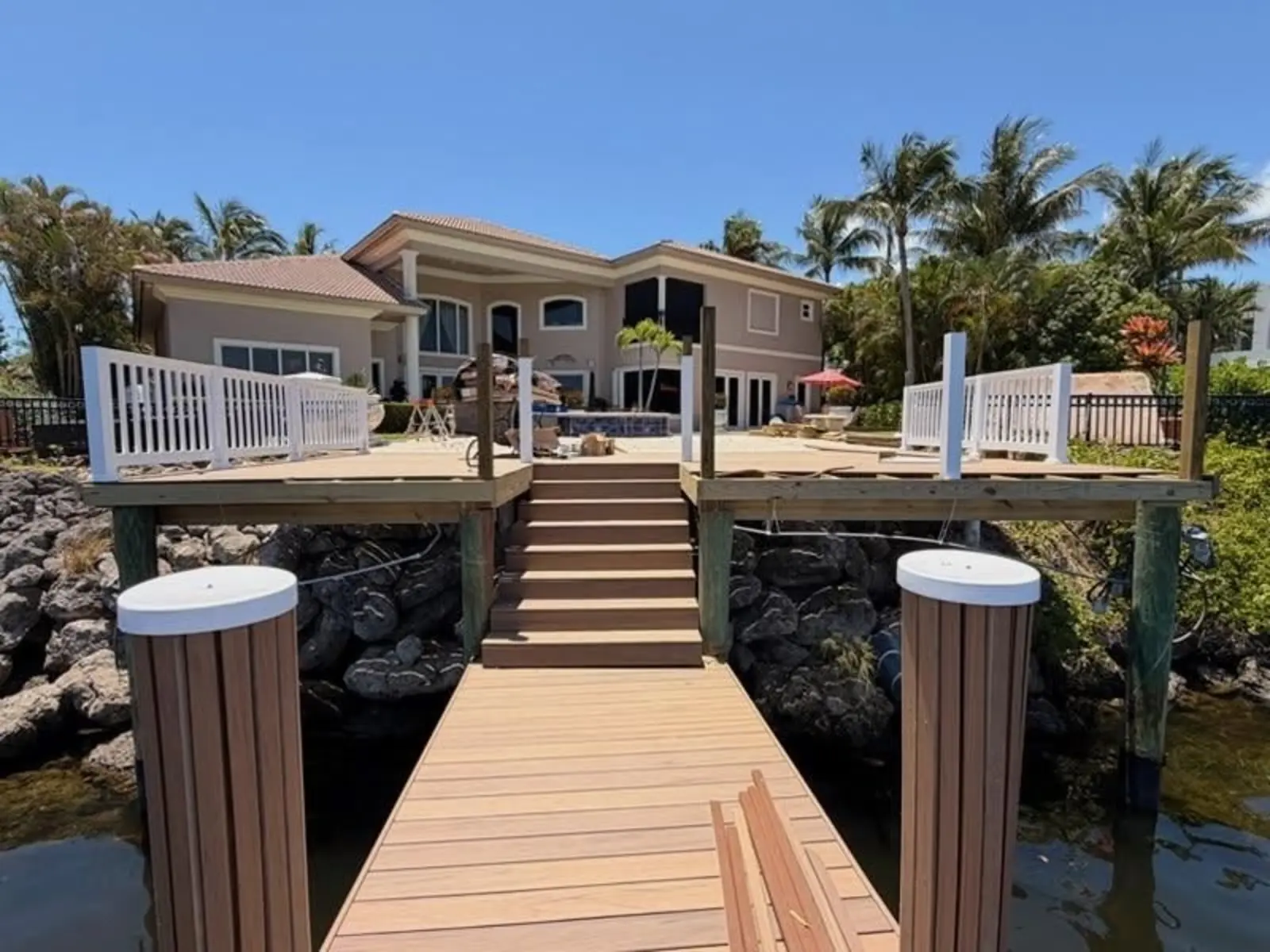 Composite dock and stairs leading to a waterfront home, with a rock shoreline of large limestone boulders on both sides of the dock